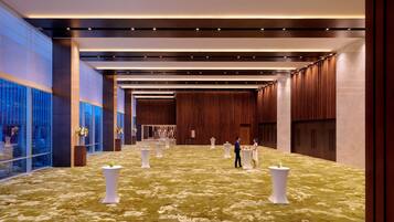 A spacious lobby with a patterned carpet, tall wooden panels, and a glass wall with a view.