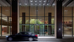 Una entrada de hotel moderna con un giratorio, fachada de vidrio y una escalera visible que conduce a los pisos superiores.
