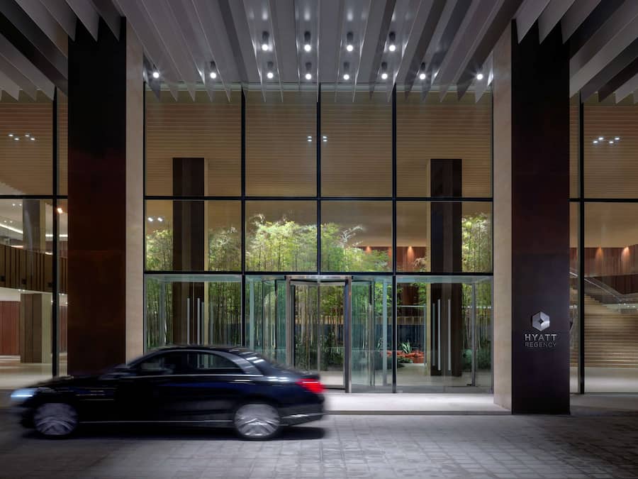 Una entrada de hotel moderna con un giratorio, fachada de vidrio y una escalera visible que conduce a los pisos superiores.