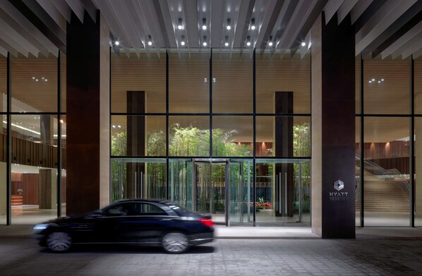 A modern hotel entrance with a revolving door, glass facade, and a visible staircase leading to the upper floors. - Hyatt Regency Beijing Wangjing (Beijing)