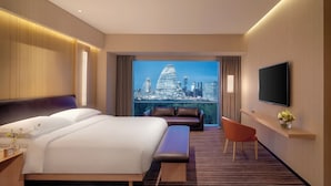 Habitación de hotel con una cama grande, un sofá, una silla, un televisor y vistas a la ciudad.