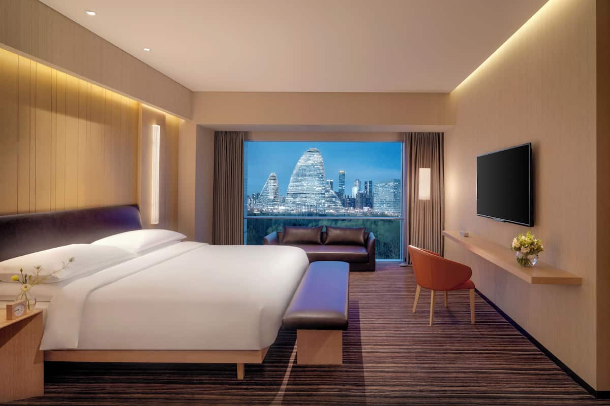 Habitación de hotel con una cama grande, un sofá, una silla, un televisor y vistas a la ciudad.