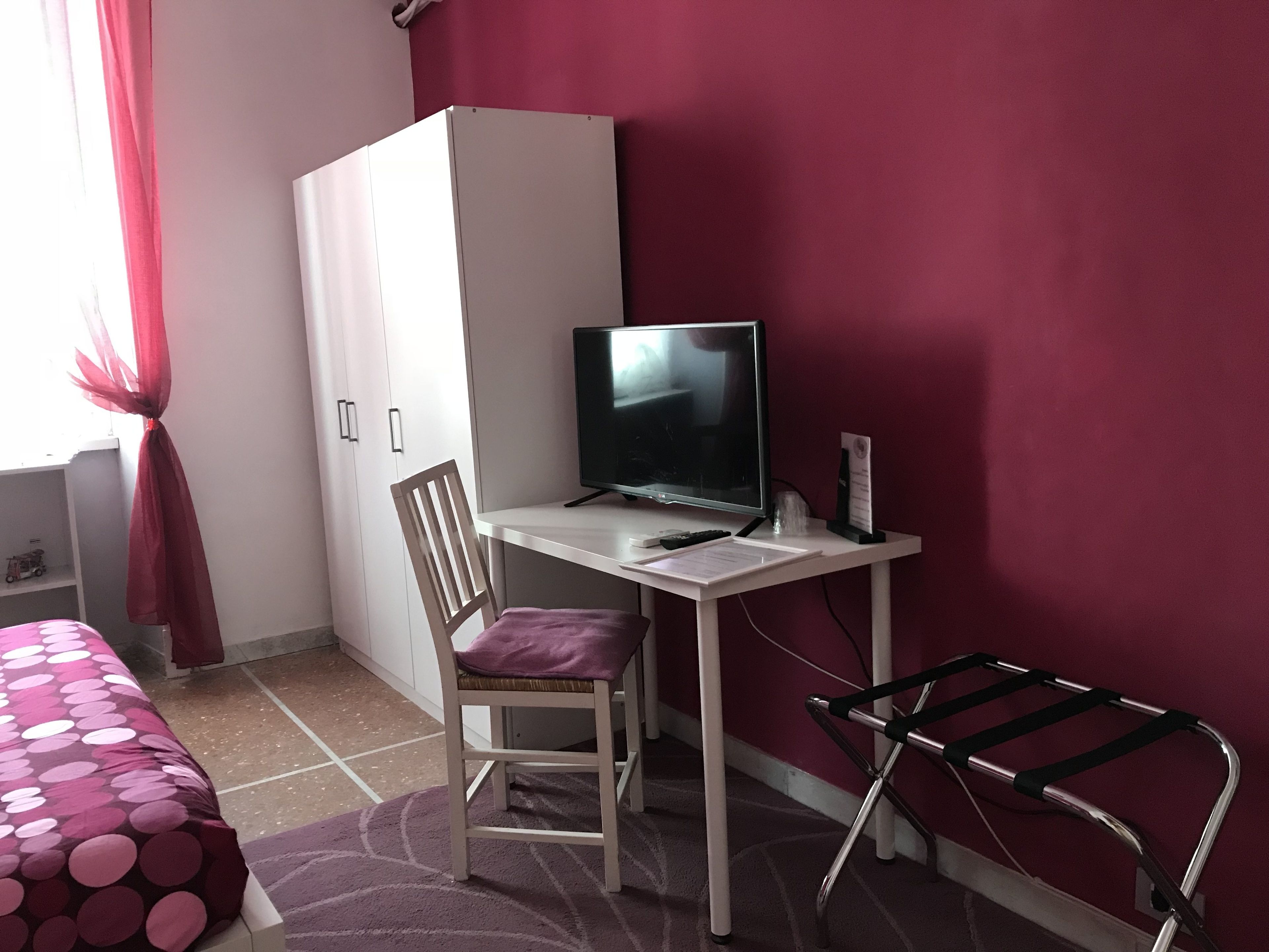 Quarto com cama, escrivaninha com computador, cadeira, guarda-roupa e janela com cortinas.