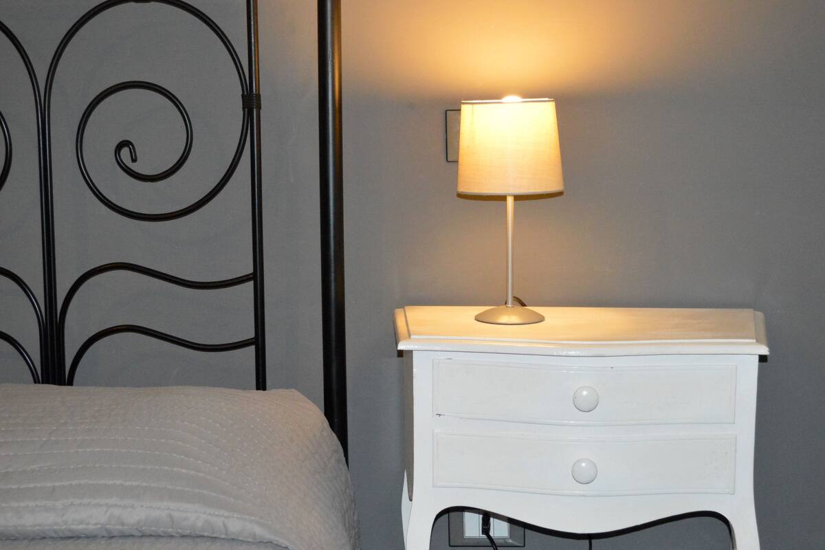 Una cama con edredón blanco y una mesita de noche blanca con una lámpara.