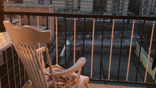 Un balcon avec un fauteuil à bascule, un sol carrelé et une vue sur un parking et des bâtiments situés au loin.