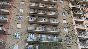 Un immeuble résidentiel à plusieurs étages, doté de balcons, de paraboles de réception par satellite et surmonté d’une grue de construction en arrière-plan.