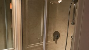 Une douche fermée par des parois de verre, avec un lavabo blanc et un miroir.