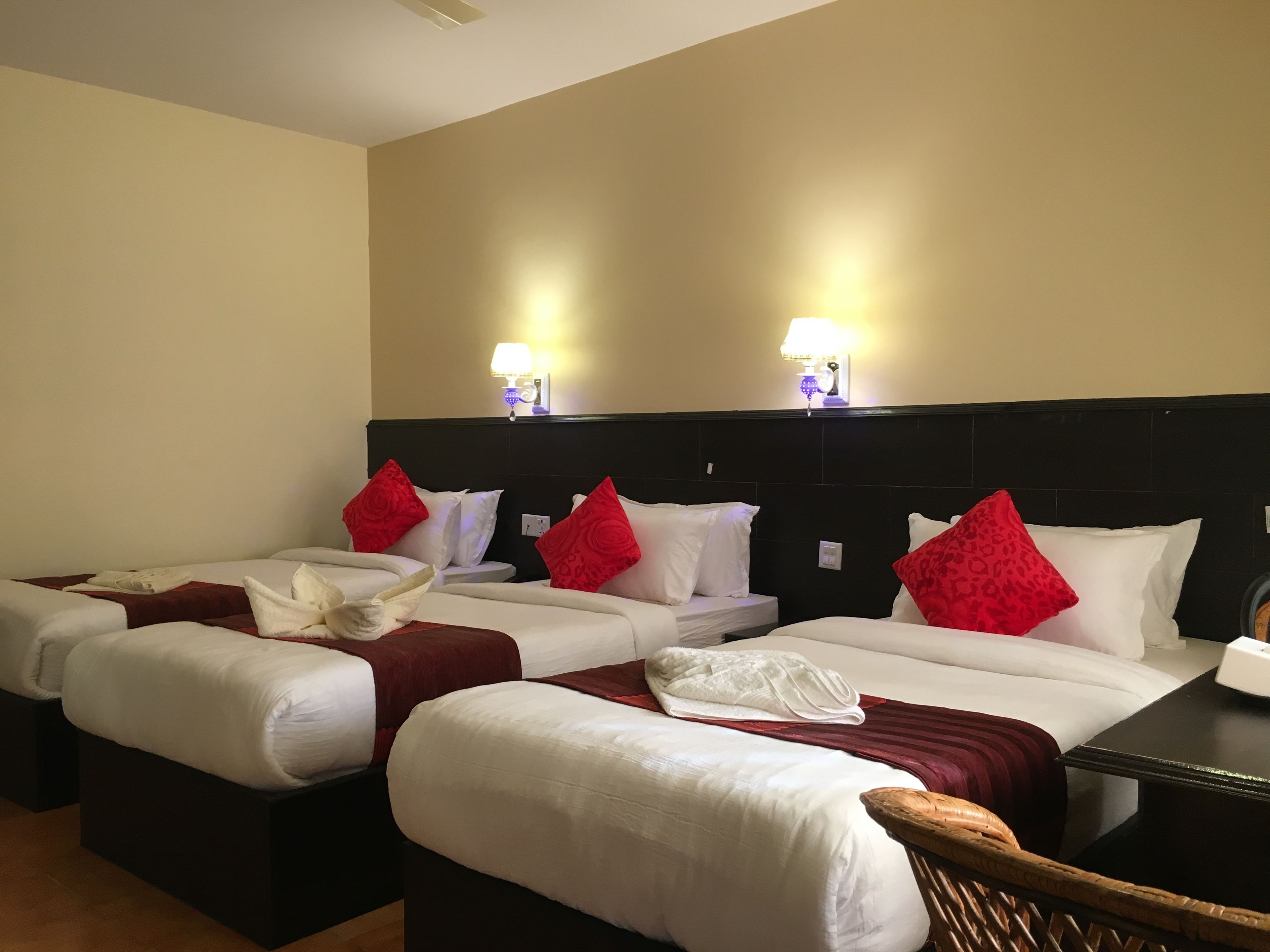 Une chambre d’hôtel avec trois lits, chacun doté de draps blancs et d’oreillers rouges, ainsi que deux lampes fixées au mur.