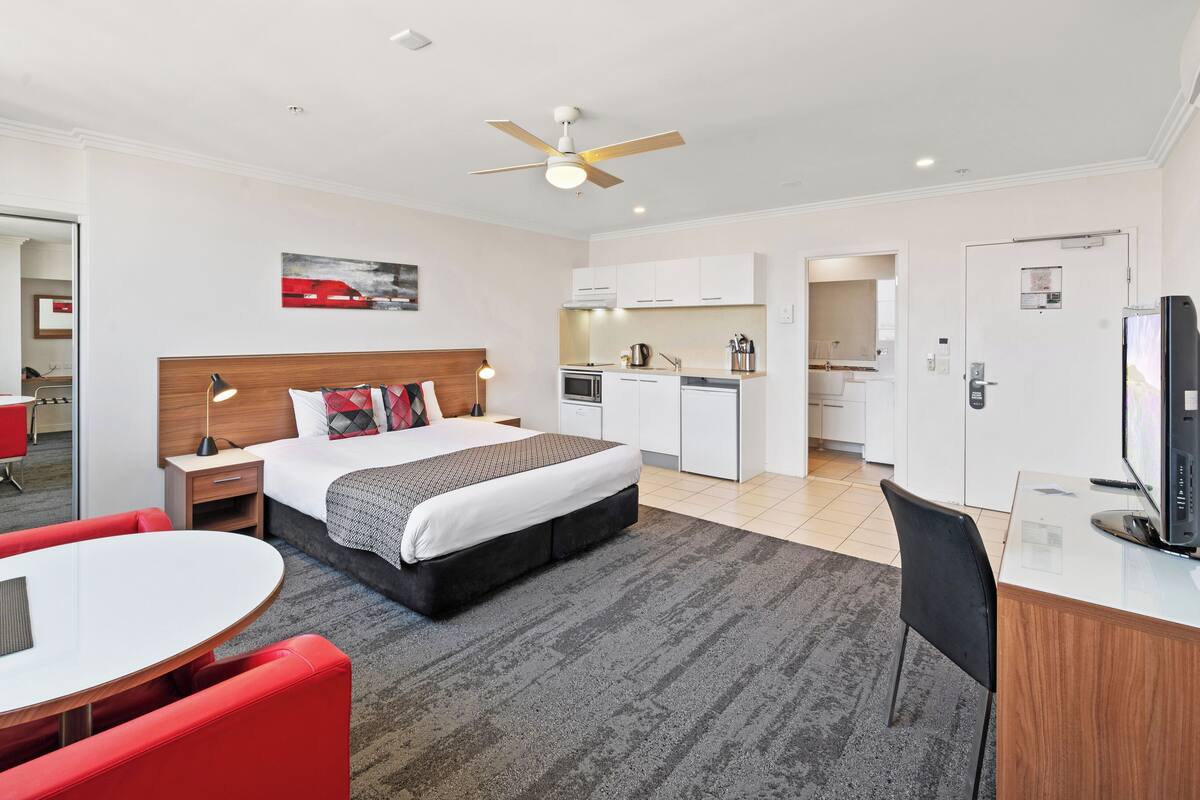 Una habitación de hotel con cama, escritorio, silla, kitchenette y comedor.