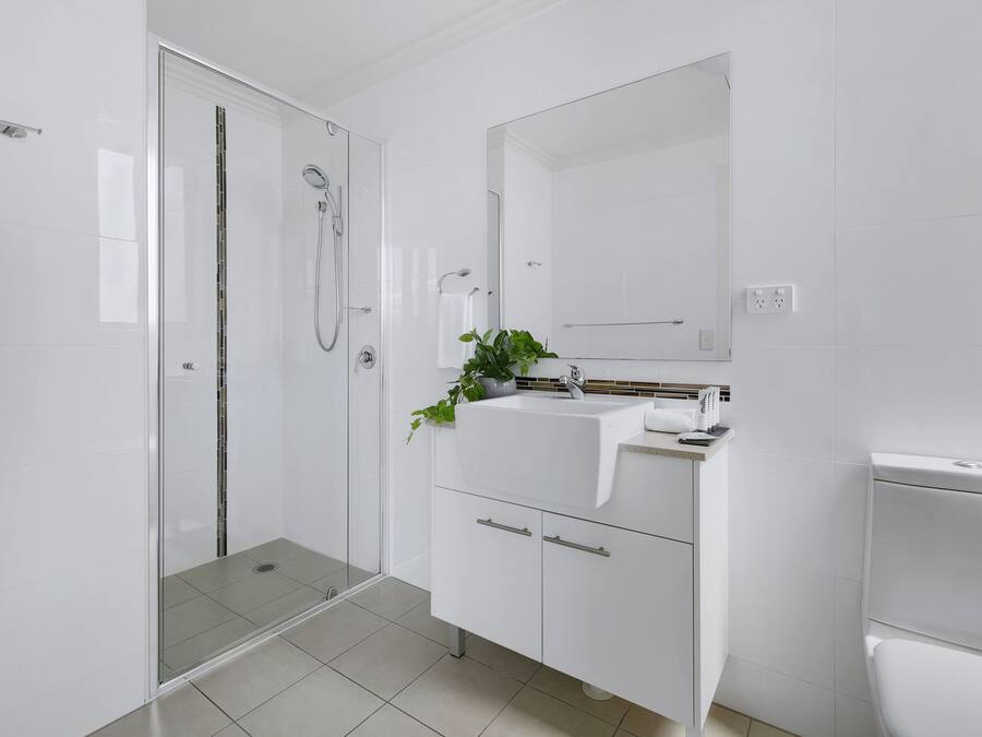 Een moderne badkamer met een douchecabine van glas, een witte wastafel met een spiegel erboven en een toilet.