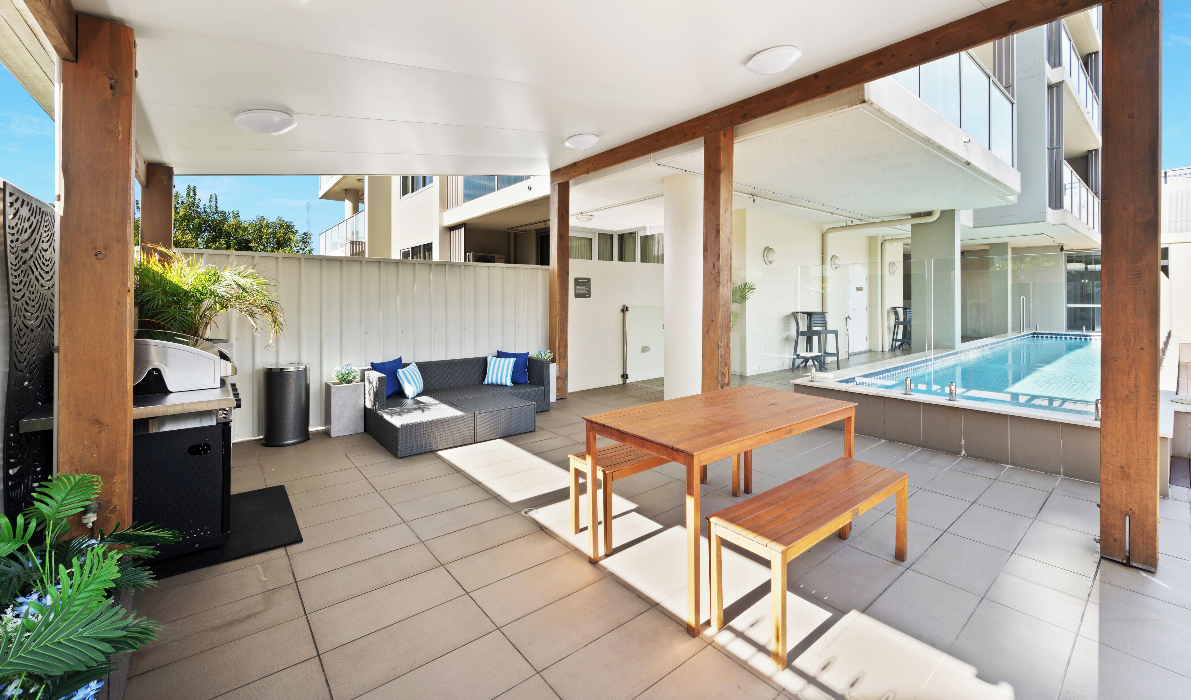 A spacious outdoor patio with a pool, a wooden table, and a sofa.