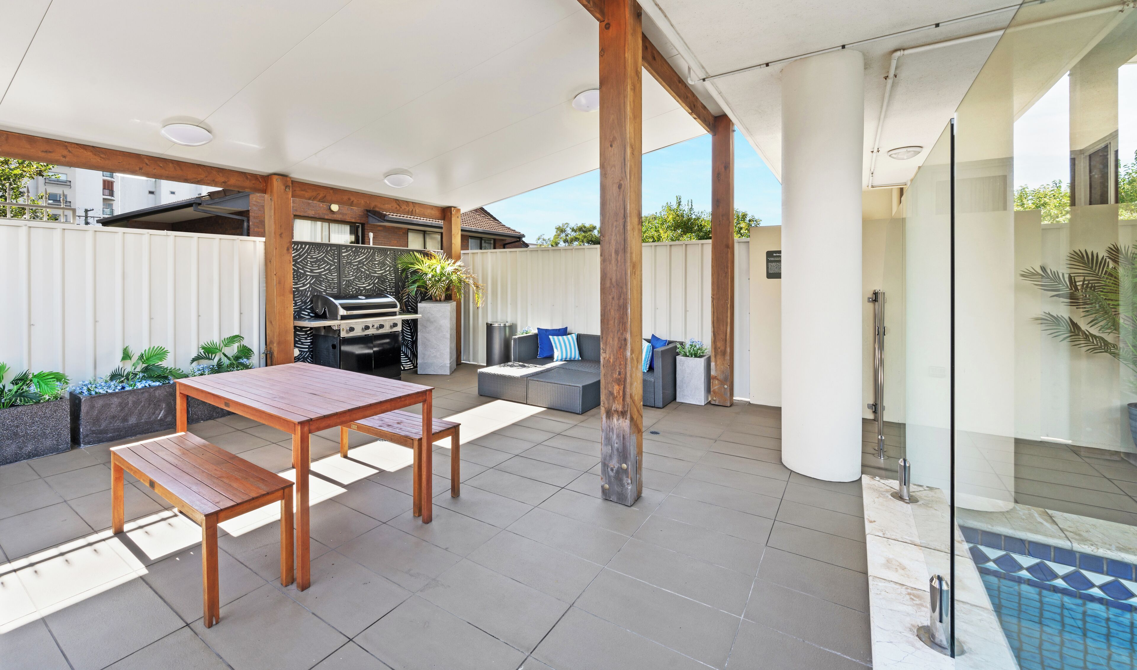 Eine Außenpatio mit Holztisch und -stühlen, einem Grill und einer Sitzecke mit Kissen.
