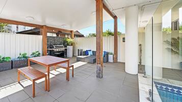 Eine Außenpatio mit Holztisch und -stühlen, einem Grill und einer Sitzecke mit Kissen.