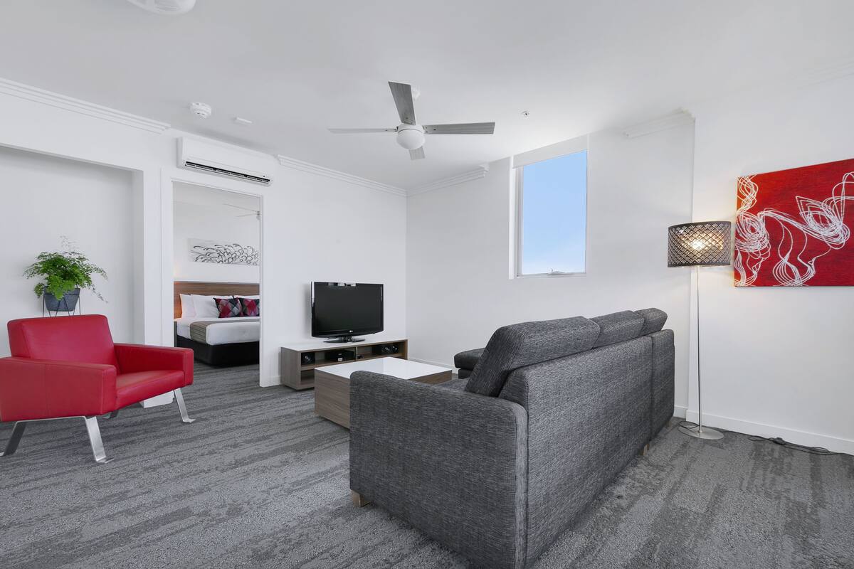 Una sala de estar moderna con un sofá gris, una butaca roja, un televisor y una lámpara de pie.
