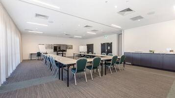 A conference room with a long table, green chairs, a whiteboard, and a projector screen.