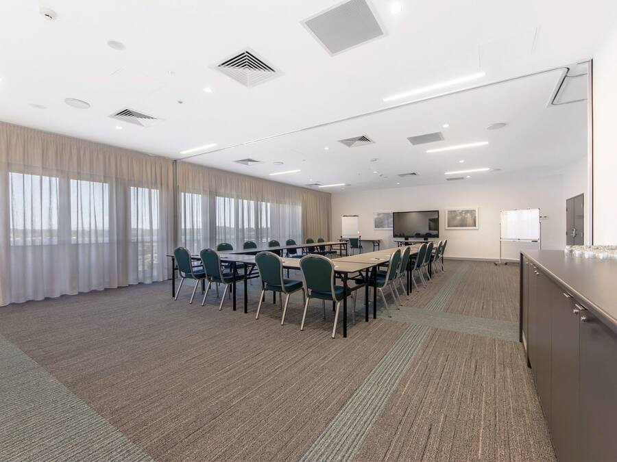 A conference room with a long table, chairs, a whiteboard, a TV, and a large window with curtains.
