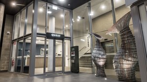 A modern hotel entrance with a 'QUEST' sign, a reception desk, and a unique spiral staircase. - Quest Midland (Midland)