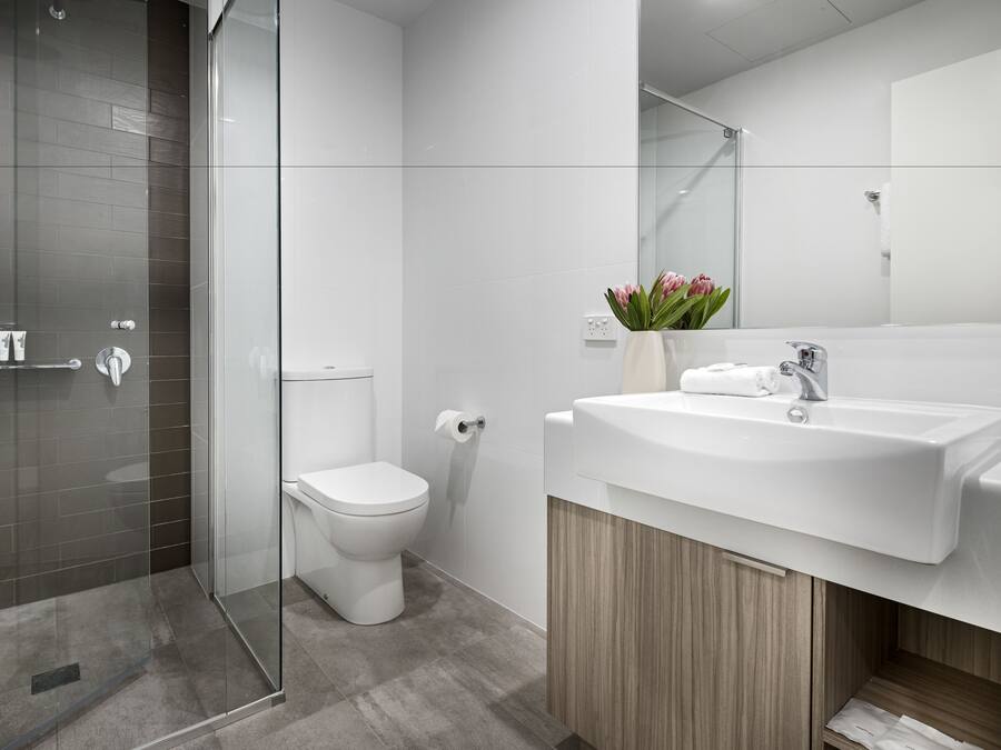 Un baño moderno con cabina de ducha de vidrio, inodoro blanco y lavabo con espejo.