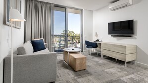 A modern hotel room with a sofa, a small table, a TV, and a balcony with a view. - Quest Midland (Midland)