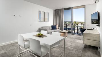 A modern hotel room with a dining area, a sofa, a TV, and a balcony with a city view.