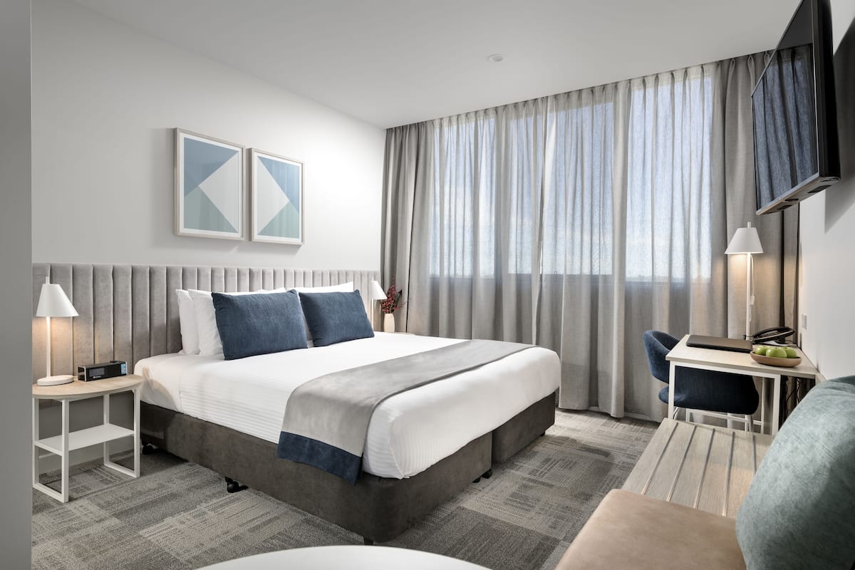 A modern hotel room with a large bed, bedside tables, a desk, and a TV.