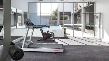 A gym with a treadmill, stationary bike, and a pool area visible through glass doors.