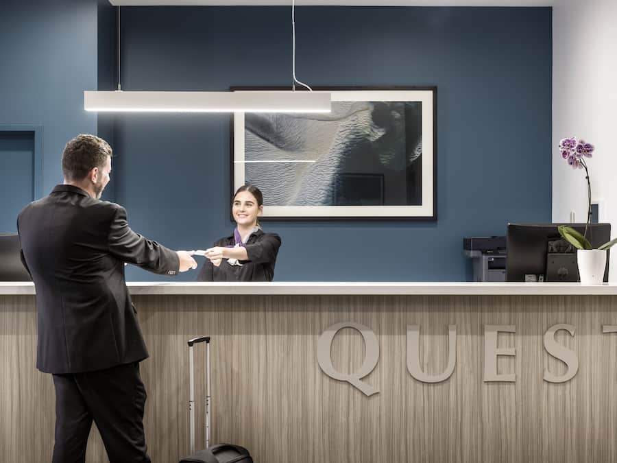 A reception desk with a modern design, a framed artwork above it, and the word "QUEST" on the wall.