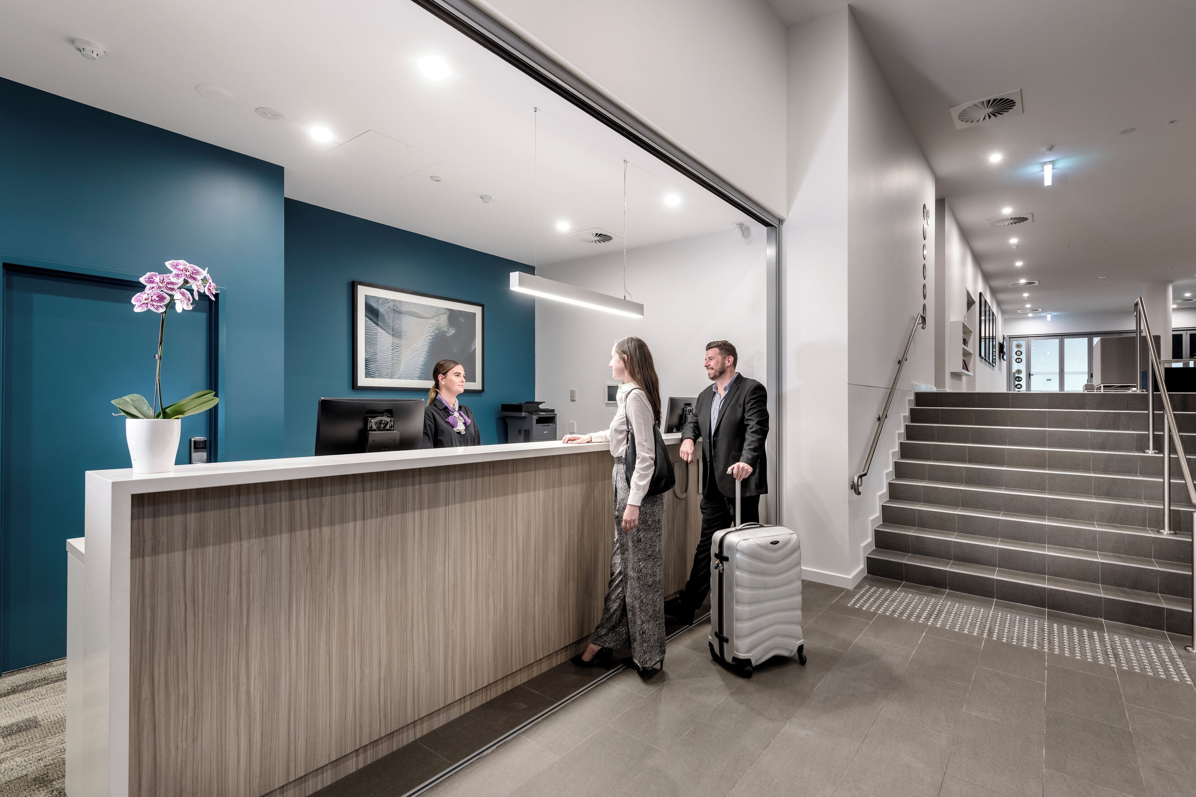 A reception area with a blue wall, a reception desk, a potted orchid, and a staircase.