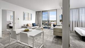 A modern hotel room with a dining area, a sofa, a bed, and a balcony with a city view. - Quest Midland (Midland)