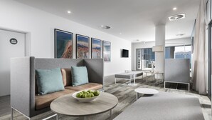 A modern hotel lobby with a grey sofa, a round table with a bowl of apples, and a view of the city through large windows. - Quest Midland (Midland)