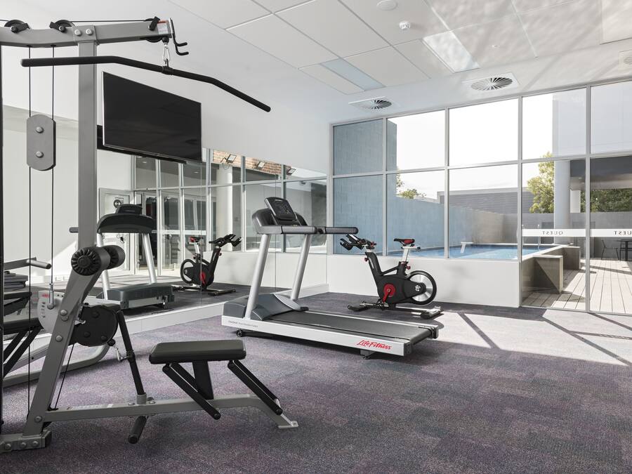 Un gimnasio moderno con equipamiento de ejercicio, un amplio ventanal y una zona de piscina.