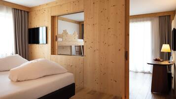 A hotel room with a wooden paneled wall, a bed with white bedding, a television mounted on the wall, and a desk with a lamp.