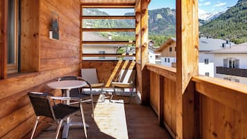 Een houten balkon met een tafel en stoelen, met uitzicht op een bergachtig landschap.