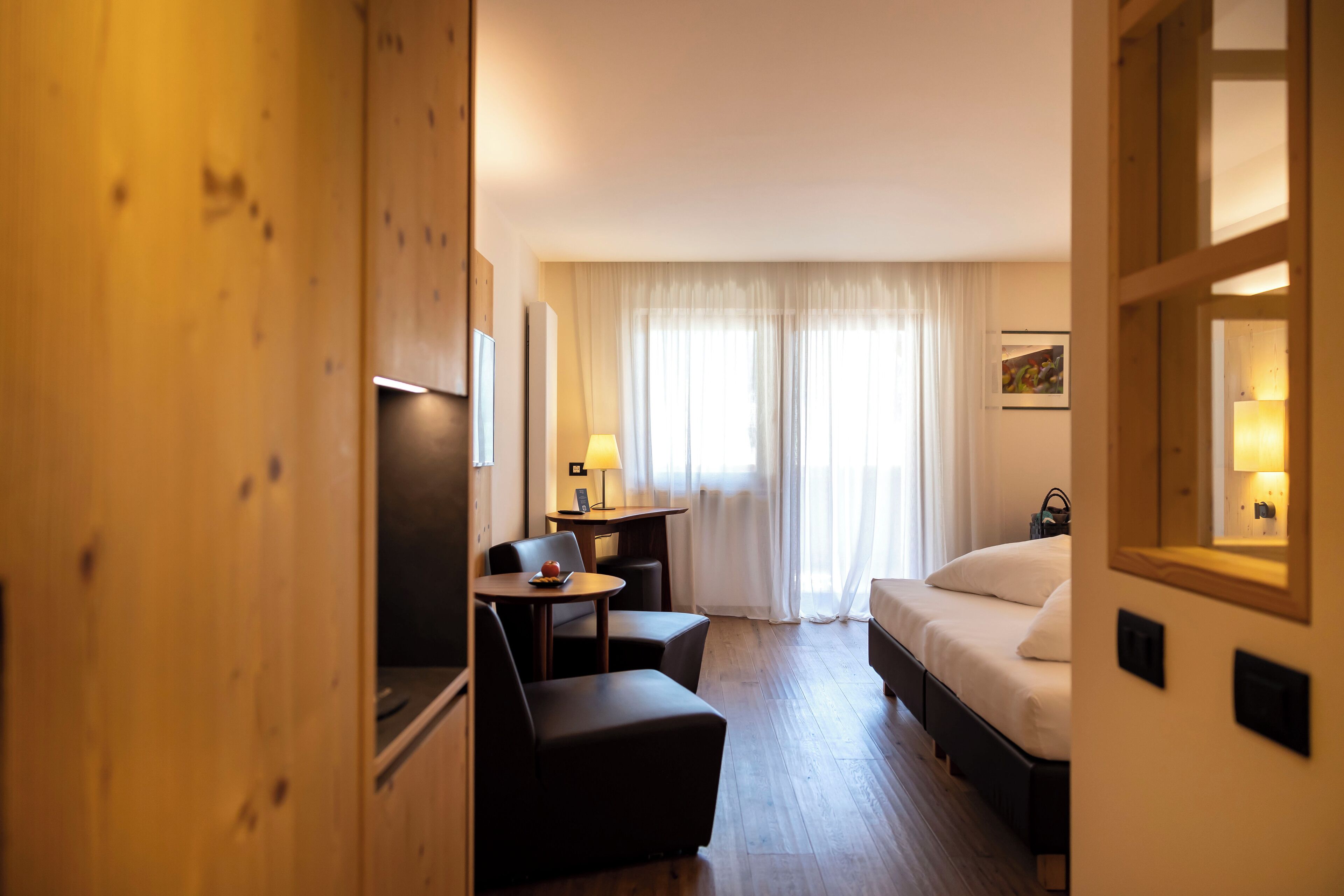 A hotel room with a bed, a desk with a lamp, a chair, and a small table.