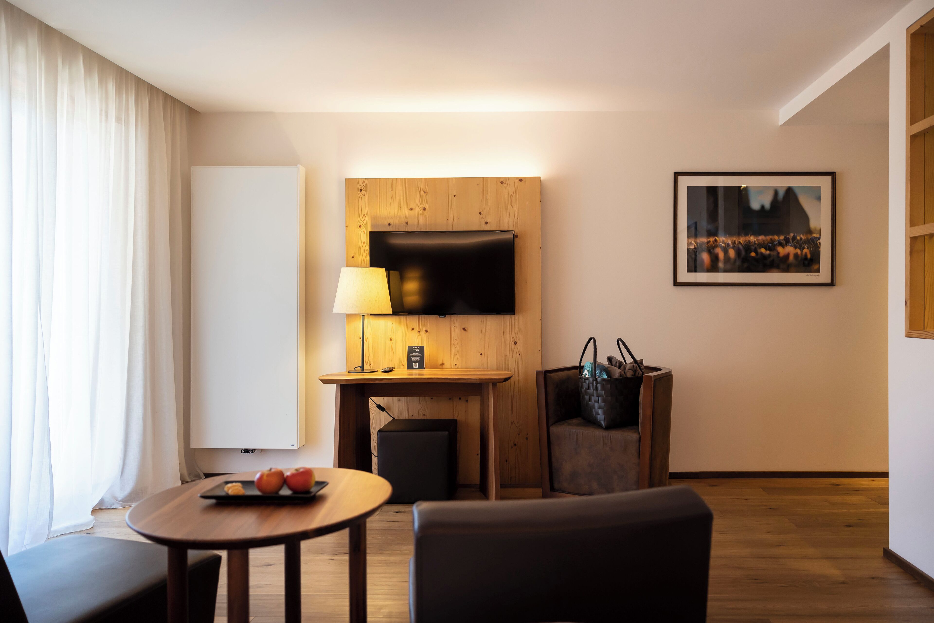 Habitación de hotel con un escritorio de madera, un televisor de pantalla plana montado en la pared, una mesa con lámpara, una silla y un sofá.