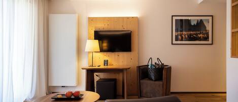 Habitación de hotel con un escritorio de madera, un televisor de pantalla plana montado en la pared, una mesa con lámpara, una silla y un sofá.