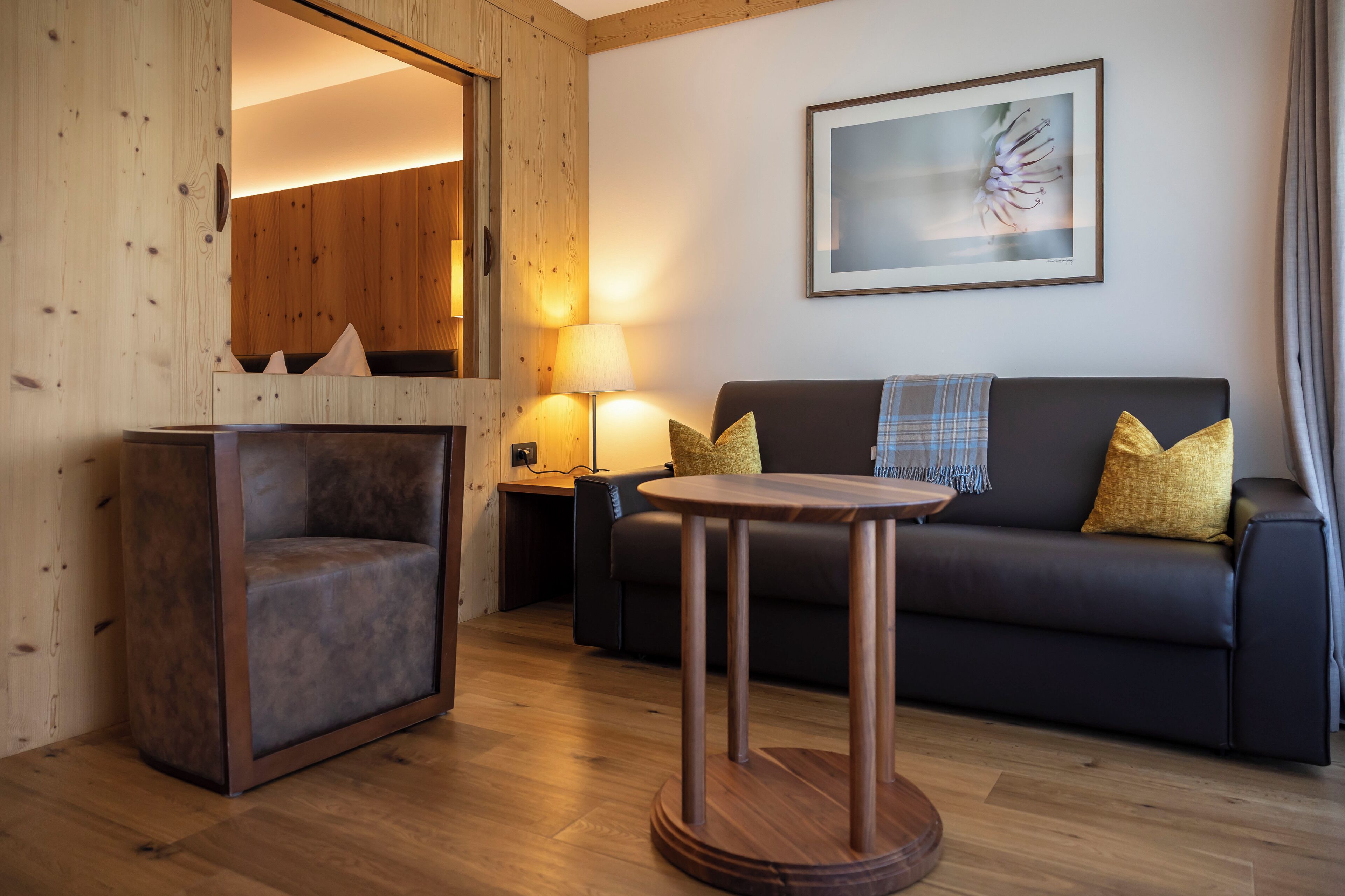 Una sala de estar moderna con piso de madera, un sofá oscuro con cojines amarillos, una mesita redonda y una lámpara.