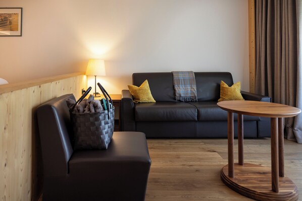Un salón moderno con un sofá negro, dos almohadas amarillas, una manta a cuadros, una mesa de centro de madera y una lámpara.
