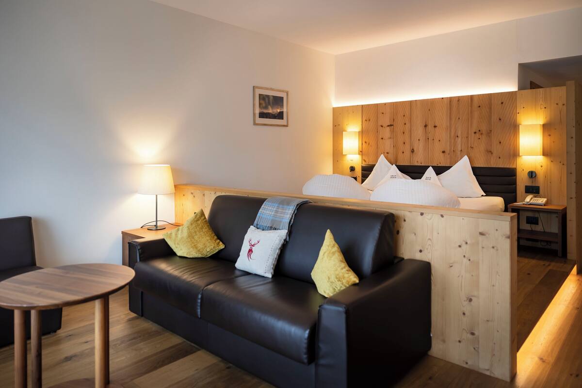 A modern hotel room with a black leather sofa, a wooden headboard, and a small table.