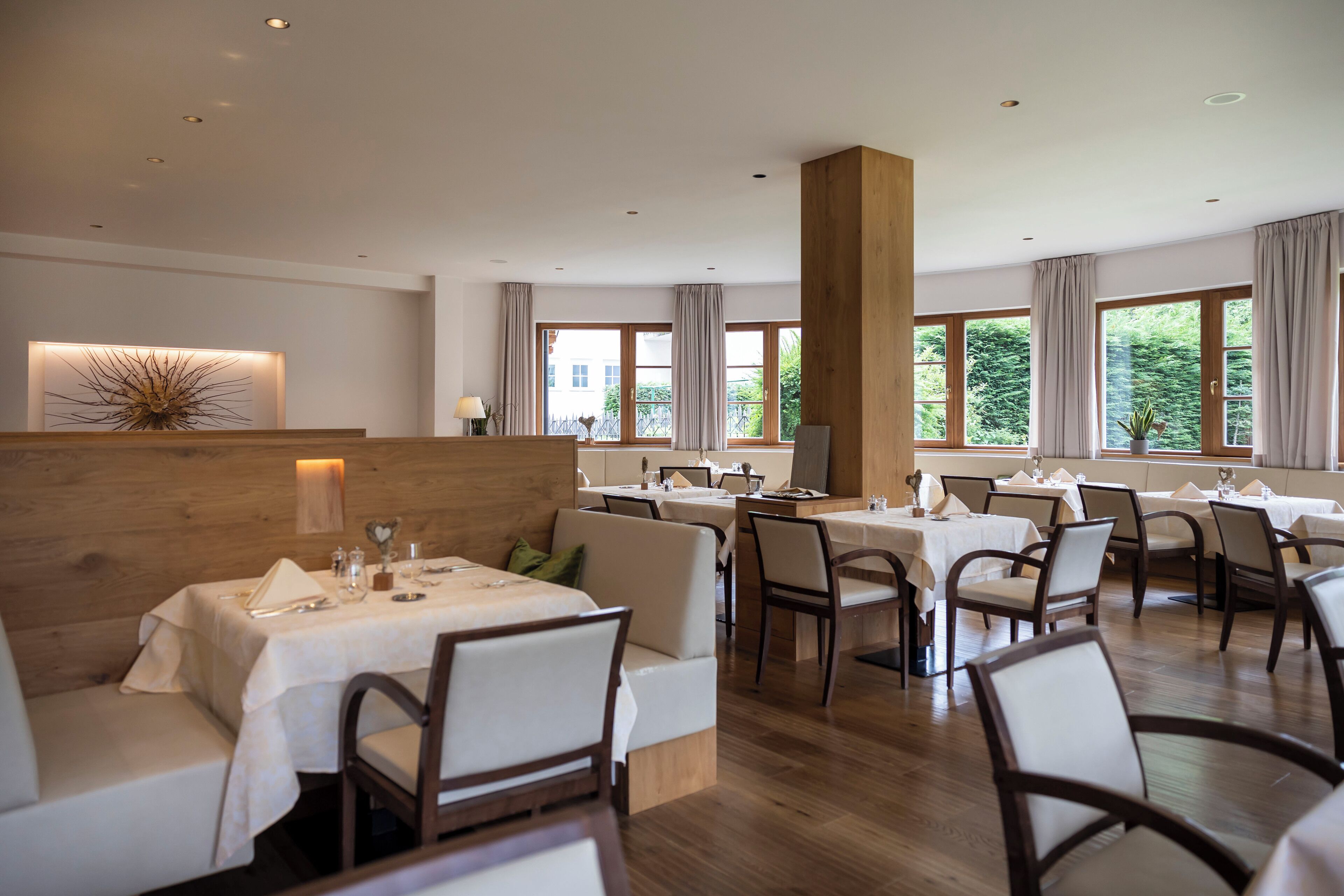 A restaurant with multiple tables and chairs, large windows with curtains, and a wooden accent wall.