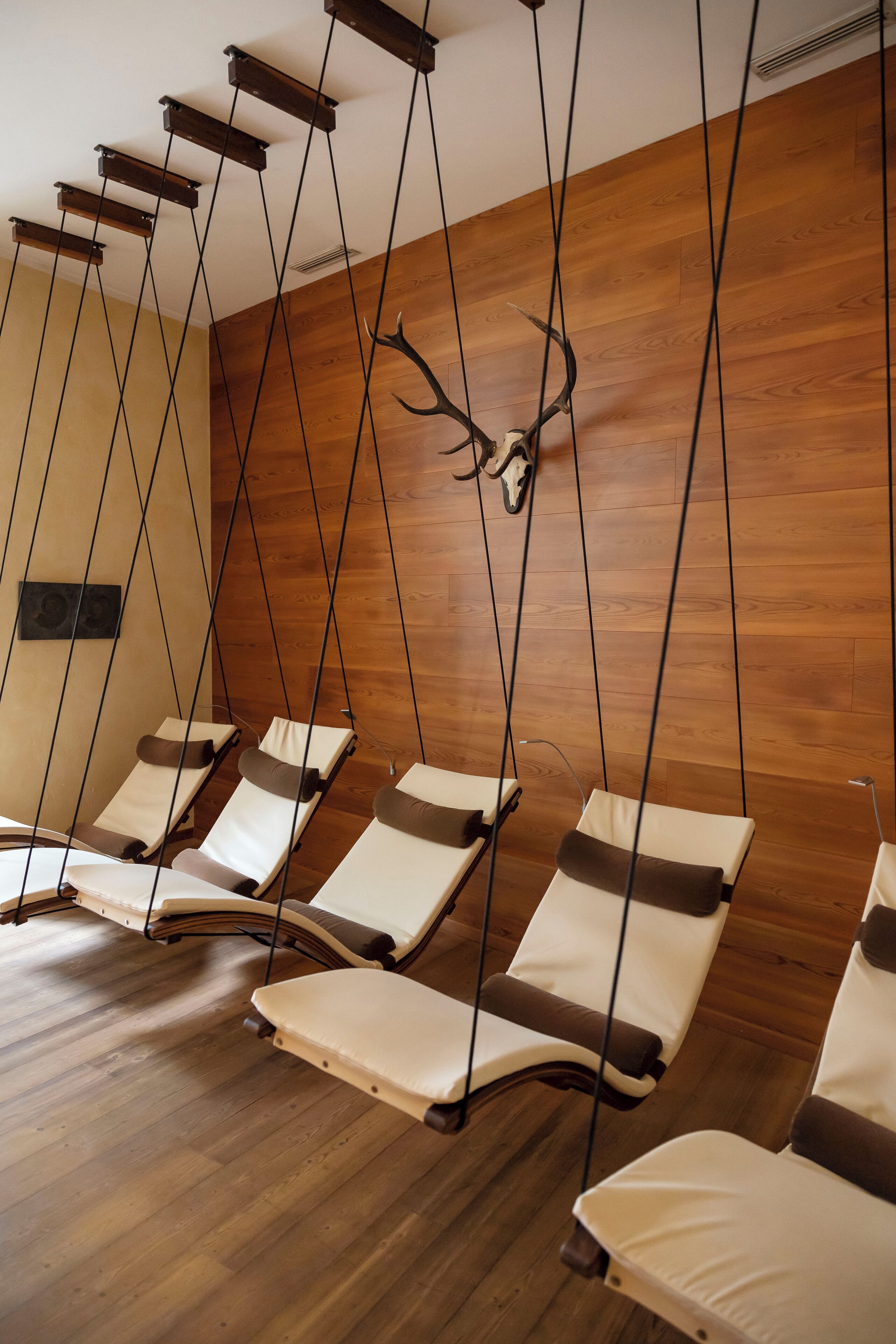 A room with wooden flooring, multiple reclining chairs, and a wall-mounted deer head sculpture.