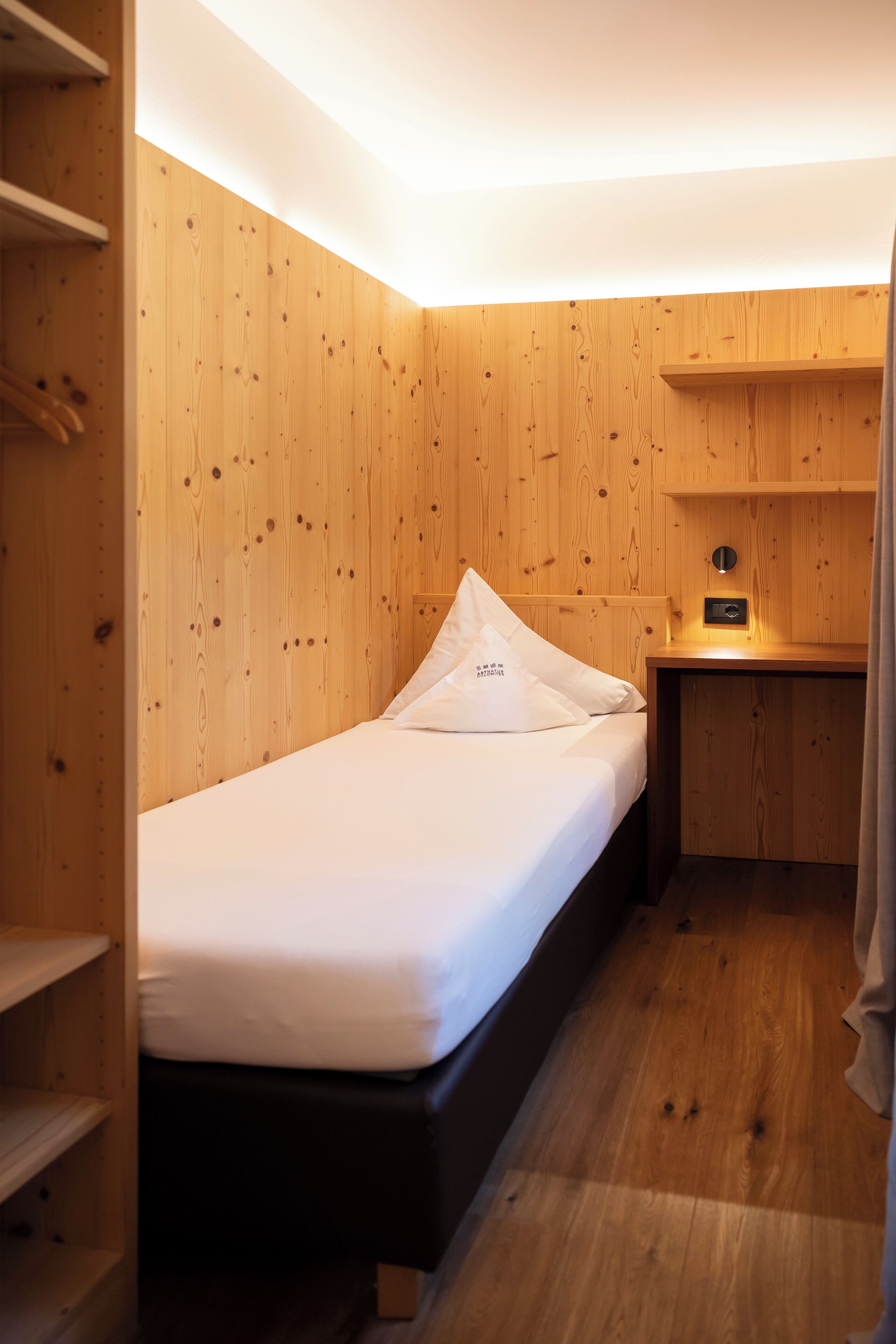 Une petite chambre à coucher, bien rangée, avec un mur en bois, un lit simple, une table de chevet et une étagère intégrée.