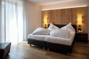 Un dormitorio moderno con cabecera de madera, una cama grande con ropa blanca, dos lámparas de noche y suelo de madera.