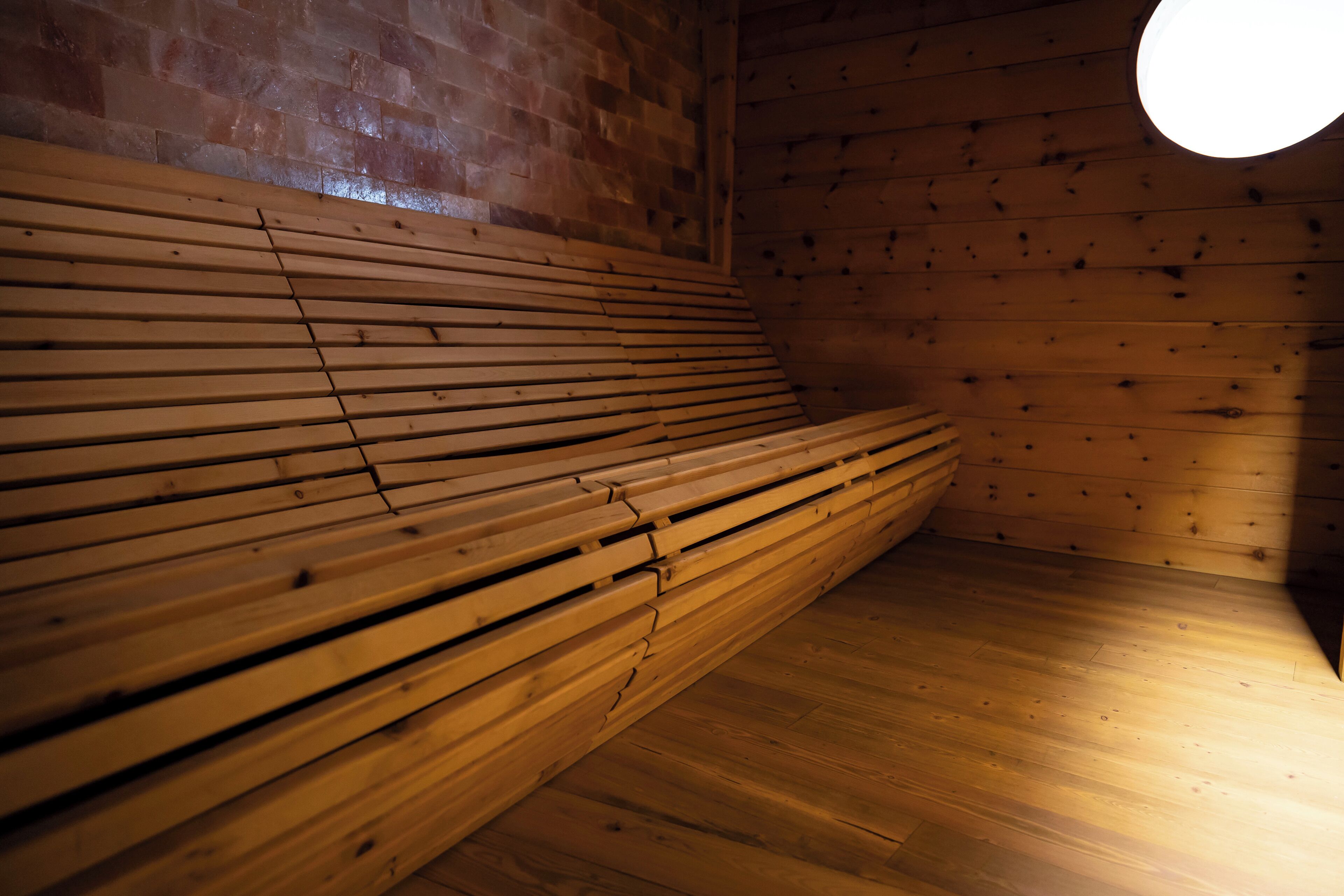 Un banco de madera con respaldo inclinado en una habitación con paredes de madera y una ventana circular.
