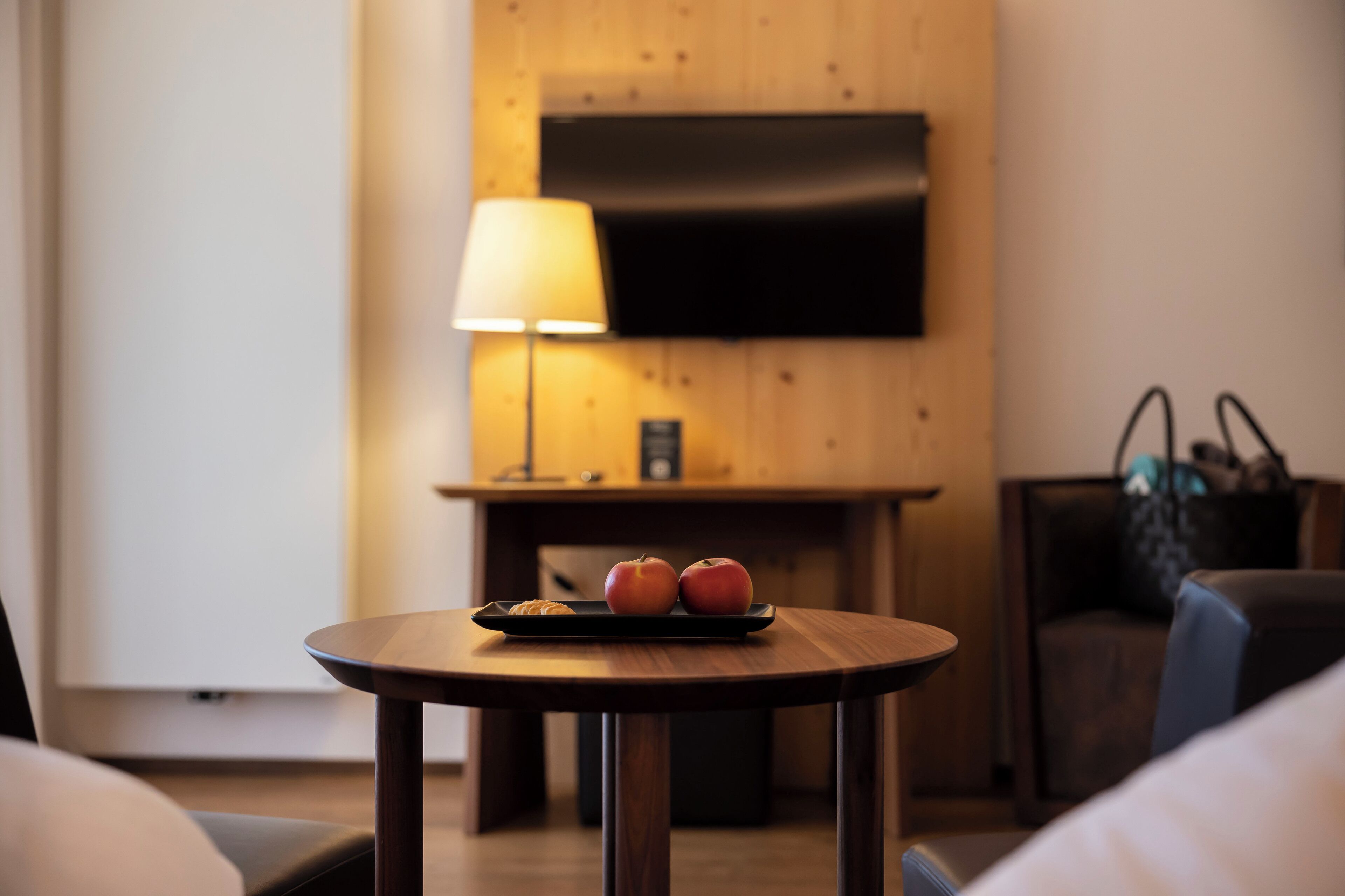 A hotel room with a wooden wall, a flat-screen TV mounted above a table with two apples and a croissant.