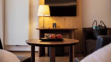 A hotel room with a wooden wall, a flat-screen TV mounted above a table with two apples and a croissant.