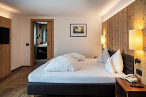 Habitación de hotel moderna con una cama grande, paneles de madera, un televisor montado y un teléfono junto a la cama.