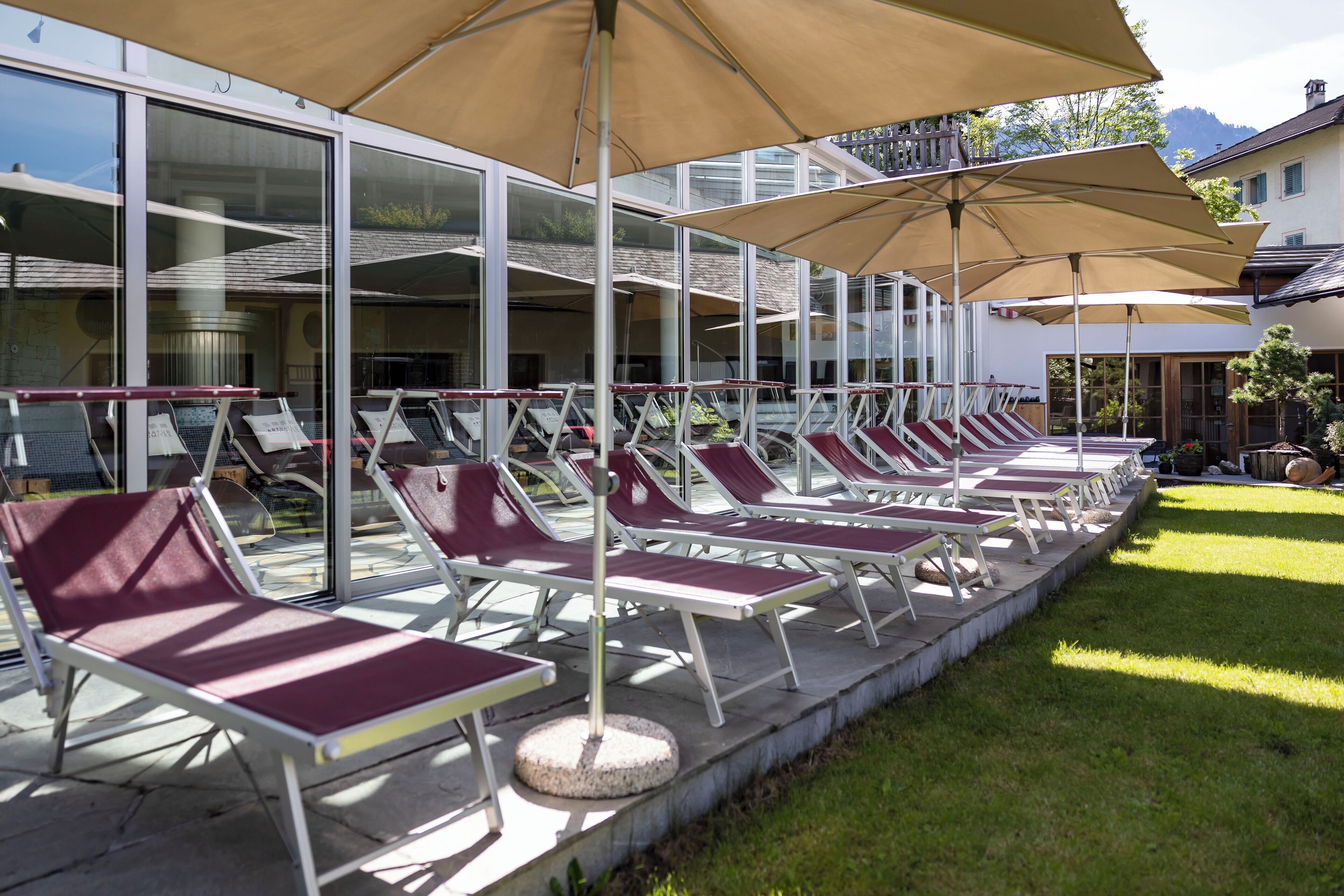 Eine Reihe von Liegestühlen mit Sonnenschirmen, ein Poolbereich und ein Gebäude mit großen Fenstern im Hintergrund.