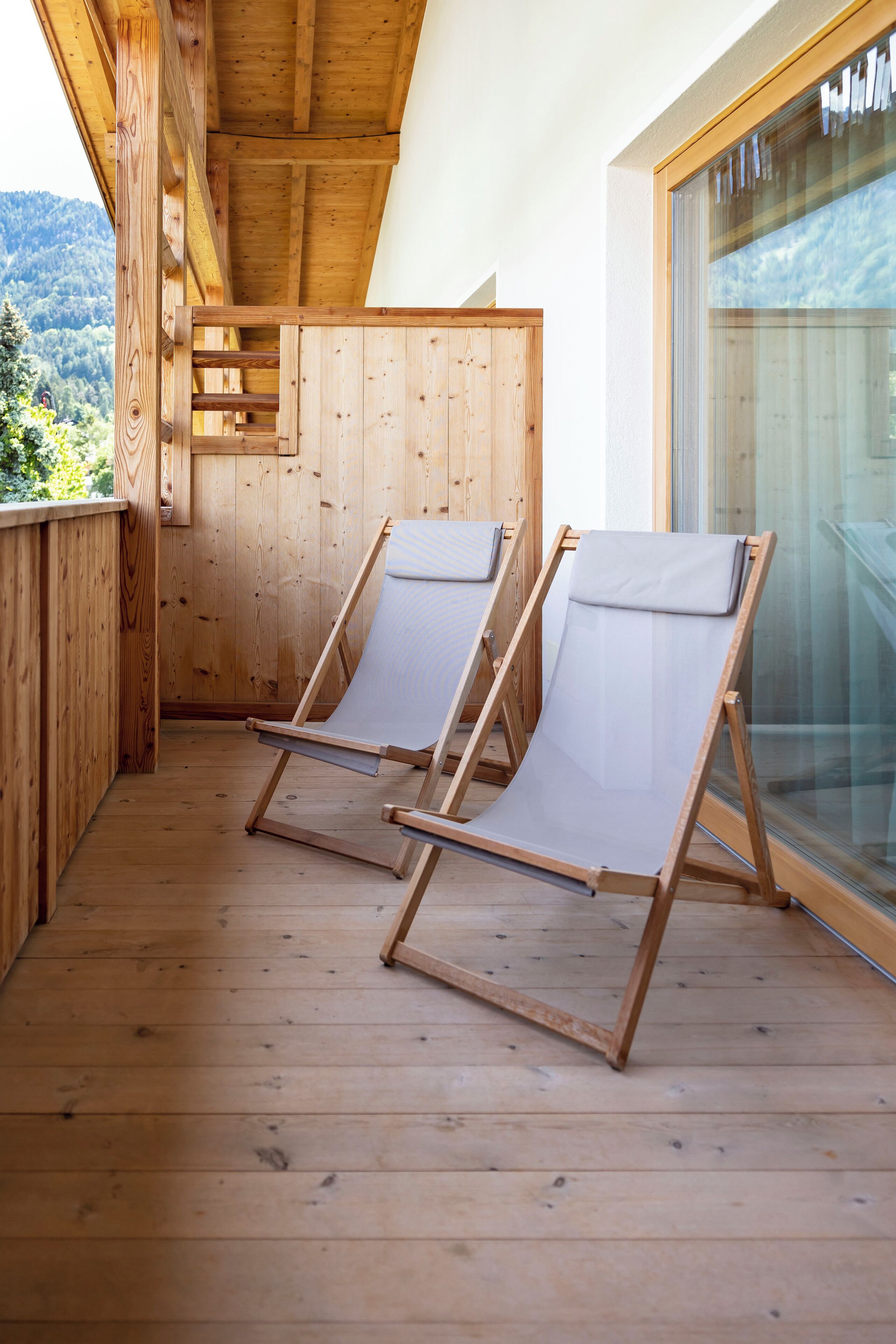 Una terraza de madera con dos sillas plegables y un portón de cristal que da a un balcón.