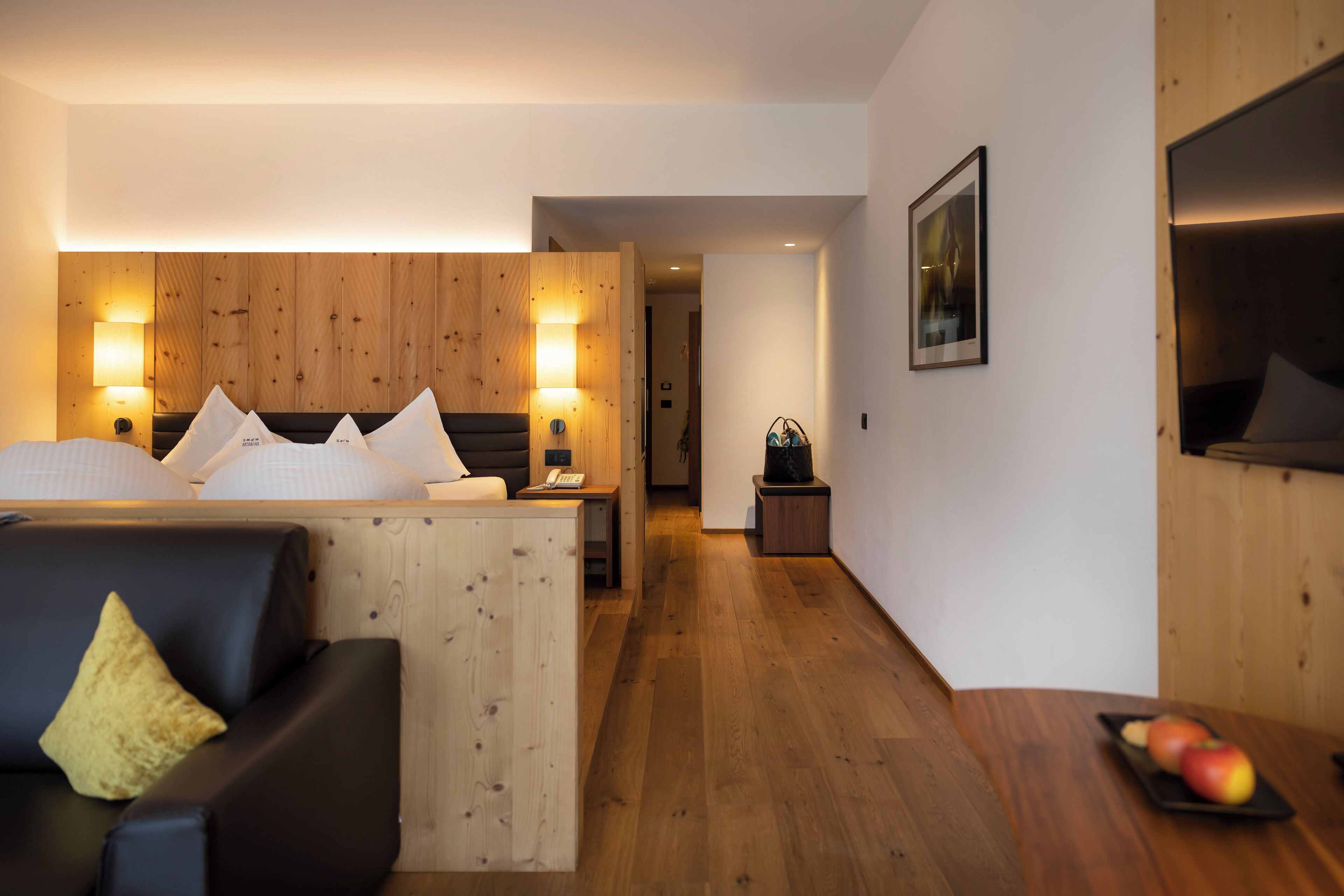 Una habitación de hotel moderna con cabecera de madera, un sofá de cuero negro, una mesa de comedor con manzanas y un mueble de madera.